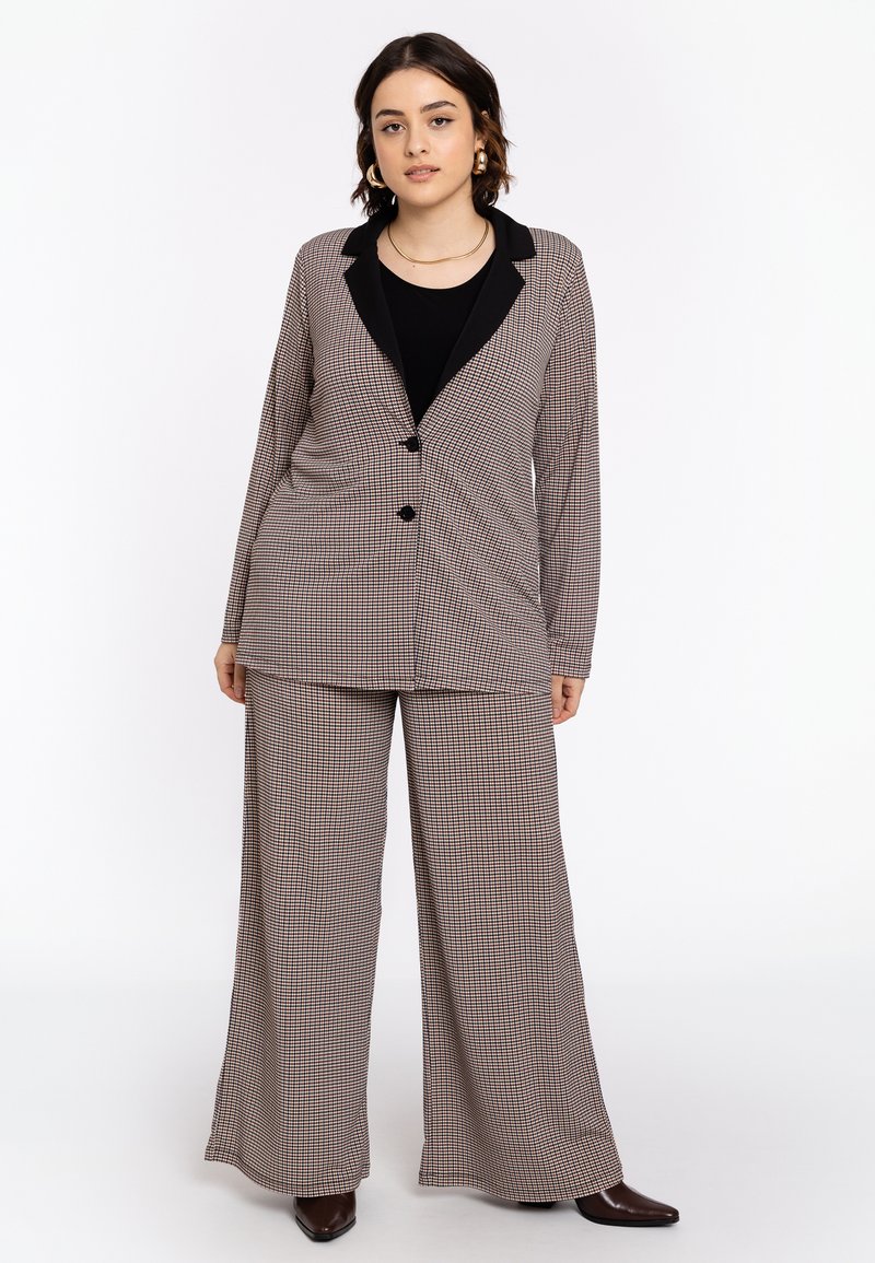 Geruit pakken in gedempte tinten met een lange blazer met zwarte revers en wijde broekspijpen, beide gemaakt van een soepele stof.