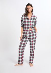 Ensemble de pyjama à carreaux en gris, rouge et vert. Chemise à boutons avec manches retroussées et pantalon droit. Tissu en coton avec une coupe décontractée.