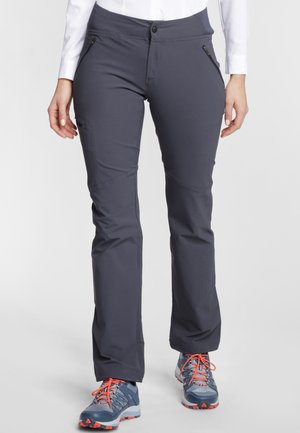 Persoon die donkergrijze outdoorbroek met ritszakken en blauwe wandelschoenen met oranje veters draagt, staand op een witte achtergrond.