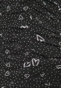 Black fabric with white polka dots and heart patterns, featuring a ruched texture. The design includes layered sections.