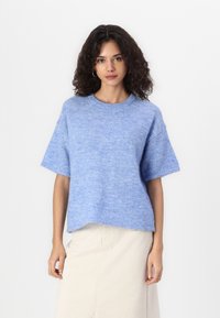 Sweater azul claro de manga curta com um corte relaxado, decote redondo e textura macia, combinado com uma saia de cor creme.
