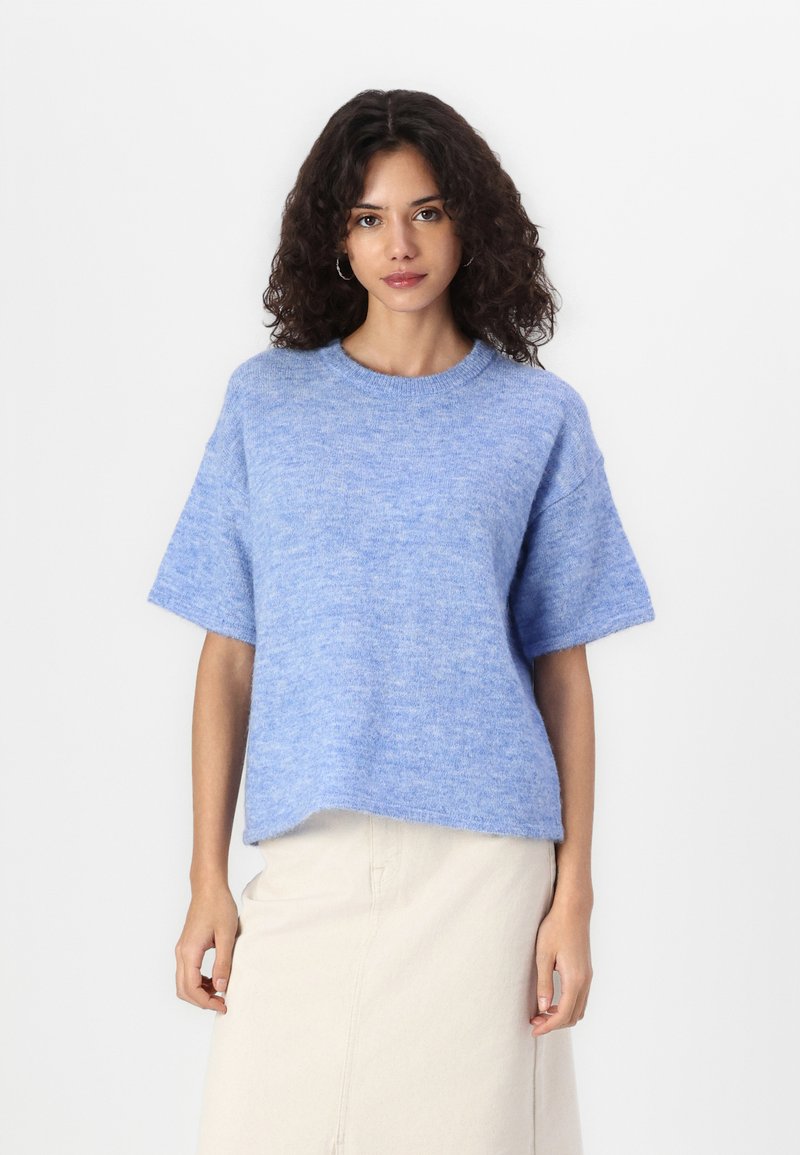Sweater azul claro de manga curta com um corte relaxado, decote redondo e textura macia, combinado com uma saia de cor creme.