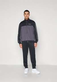 Herretreningsdrakt i mørkegrå og svart, med en glidelåsjakke med fargeblokkering og hvit logo. Buksene er matchende, med et minimalistisk design.