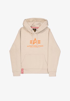 Beige kapucnis pulóver kenguruzsebbel, narancssárga "ALPHA INDUSTRIES" logós felirattal, húzózsinórral ellátott kapucnival, és piros márkajelzéssel a bal alsó szegélynél.