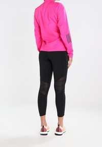 Veste de sport rose avec col montant et leggings noirs à panneaux en maille. Les chaussures ont un accent rose et une semelle blanche.