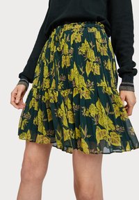 Jupe plissée fleurie en vert foncé avec des motifs jaunes et marron. Taille élastique avec cordon de serrage, design superposé et texture transparente.