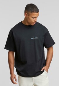 Tricou din bumbac negru, cu mâneci scurte, decolteu rotund. Prezintă un mic logo "Another Cotton" în albastru pe partea stângă a pieptului.