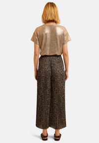 Glanzend gouden, geribbelde top met korte mouwen, gecombineerd met zwarte, geplooide, bloemenpatroon wijd-uitlopende broeken. Comfortabele pasvorm met een relaxte silhouette.