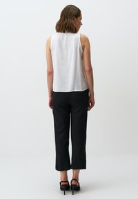 Top bianco senza maniche realizzato in tessuto leggero, abbinato a pantaloni neri a vita alta. Tacchi neri completano l'outfit. Design semplice e moderno.