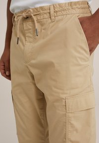 Beige cargo byxor av lättviktig tyg med elastisk midja och dragsko. Har sidofickor och en ficka på benet.