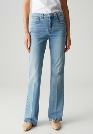 Lichtblauwe, flare jeans van denim. Heeft een knoopsluiting, vijf zakken en een vervaagde textuur. Gecombineerd met nude schoenen.