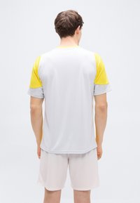 Άσπρο αθλητικό πουκάμισο με κίτρινες και γκρι μανσέτες, και ταιριαστό ανοιχτόχρωμο σορτς. Λείο ύφασμα, σχέδιο με λαιμόκοψη και άνετη εφαρμογή.