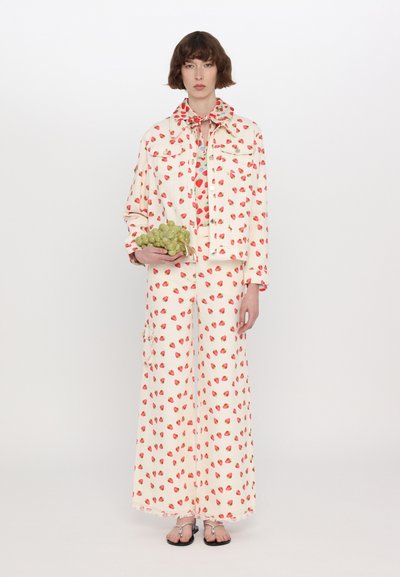 White denim jacket and wide-leg pants featuring a red strawberry print. Model holds green grapes; outfit includes a matching collar scarf.