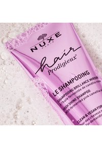 Lila Shampoo-Tube mit schwarzer Schrift, glänzender Oberfläche und Blasenakzenten, beschriftet mit "Hair Prodigieux" und "Le Shampooining."
