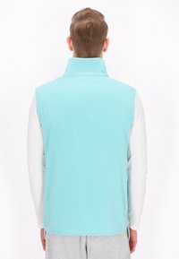 Hellblaues ärmelloses Fleece-Westen mit hohem Kragen, glatter Textur und schlichtem Design, getragen über einem langärmeligen weißen Hemd.
