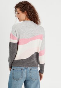 Grå, rosa og hvid stribede sweater med en blød tekstur, rund halsudskæring og lange ærmer, parret med blå denim jeans.