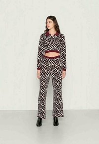 Jaqueta com padrão de zebra cortada, com colarinho bordô e calças de cintura alta combinando, ambas feitas de tecido suave. Modelo usa botas pretas.