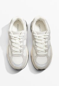 Svijetlo sivi tenisice izrađene od kombinacije tekstila i gamoša. Imaju pertlanje, podstavljeni ovratnik i boju đona u off-white nijansi.