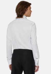 Chemise blanche �à manches longues avec un design sobre au dos, dotée d'un col classique et de boutons noirs sur les poignets. Coupe ajustée.