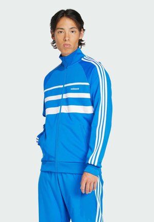 Blauer Sportanzug mit weißen Streifen an den Ärmeln und der Brust. Mit einem Reißverschluss und seitlichen Taschen. Leichtes, glattes Material.