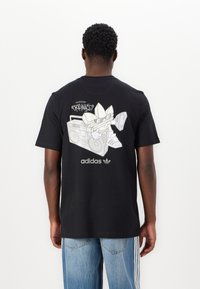 Melns kokvilnas T-krekls ar grafiku, kurā attēlots multfilmu varonis ar boomboksu, un adidas zīmols baltā krāsā priekšā un aizmugurē.