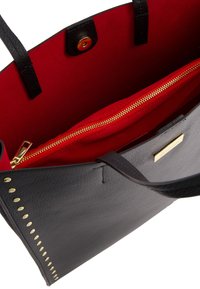 Sac fourre-tout en cuir noir avec des accents en clous dorés et un intérieur rouge. Dispose d'un compartiment zippé et d'une plaque en logo dorée.