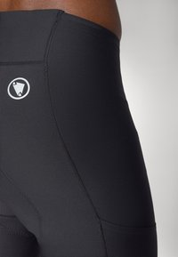 Schwarze Sportshorts aus glattem Material, mit hohem Taillenbund und einem weißen Logo-Detail an der Seitennaht. Mit Flachnaht-Stich.