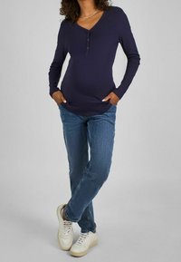 Tmavě modré dlouhé rukávy ribbed top s výstřihem do V a detaily knoflíků, kombinovaný se světle modrými džíny a bílými teniskami. Zaměření na ležérní styl.