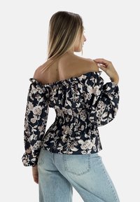 Blomsterprint off-shoulder bluse med flæset halsudskæring, sort stof og beige blomster mønstre. Har elastisk smock ved taljen.