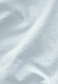 Lys blå stof med en glat, let struktureret overflade. Materialet virker let og falder blødt med subtile farvevariationer.