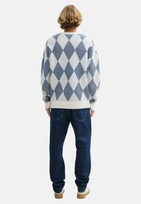 Stickad tröja i krämfärg med blått rutmönster, lös passform, ribbade muddar, matchad med blå jeans och ljusa skor.