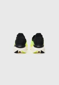 Zapatillas de correr negras y amarillas neón con un talón texturizado negro, una entresuela blanca y un logo en la parte trasera. Diseñadas para ofrecer comodidad con un estilo deportivo y elegante.