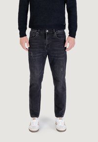 Jeans in denim nero con un leggero effetto usato, dotati di cinque tasche, chiusura a bottoni e dettagli consumati sulle ginocchia. Abbinati a sneaker bianche.
