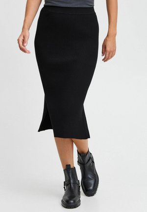 Jupe midi noire côtelée avec une silhouette ajustée et une fente latérale. Associée à des bottines noires avec des accents de boucles.