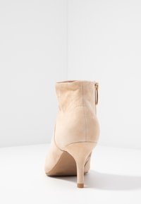 Botín de ante nude con tacón de aguja, punta redondeada y cremallera lateral. Textura suave y diseño sin costuras.