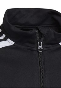 Sort zip-jacket til sport med høj krave, prydet med hvide striber og struktureret stof. YKK lynlås detalje synlig.