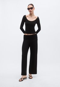 Μαύρο τοπ με μακριά μανίκια και στρογγυλή λαιμόκοψη, σε συνδυασμό με χαλαρά μαύρα παντελόνια με ελαστική μέση και μίνιμαλ σανδάλια.