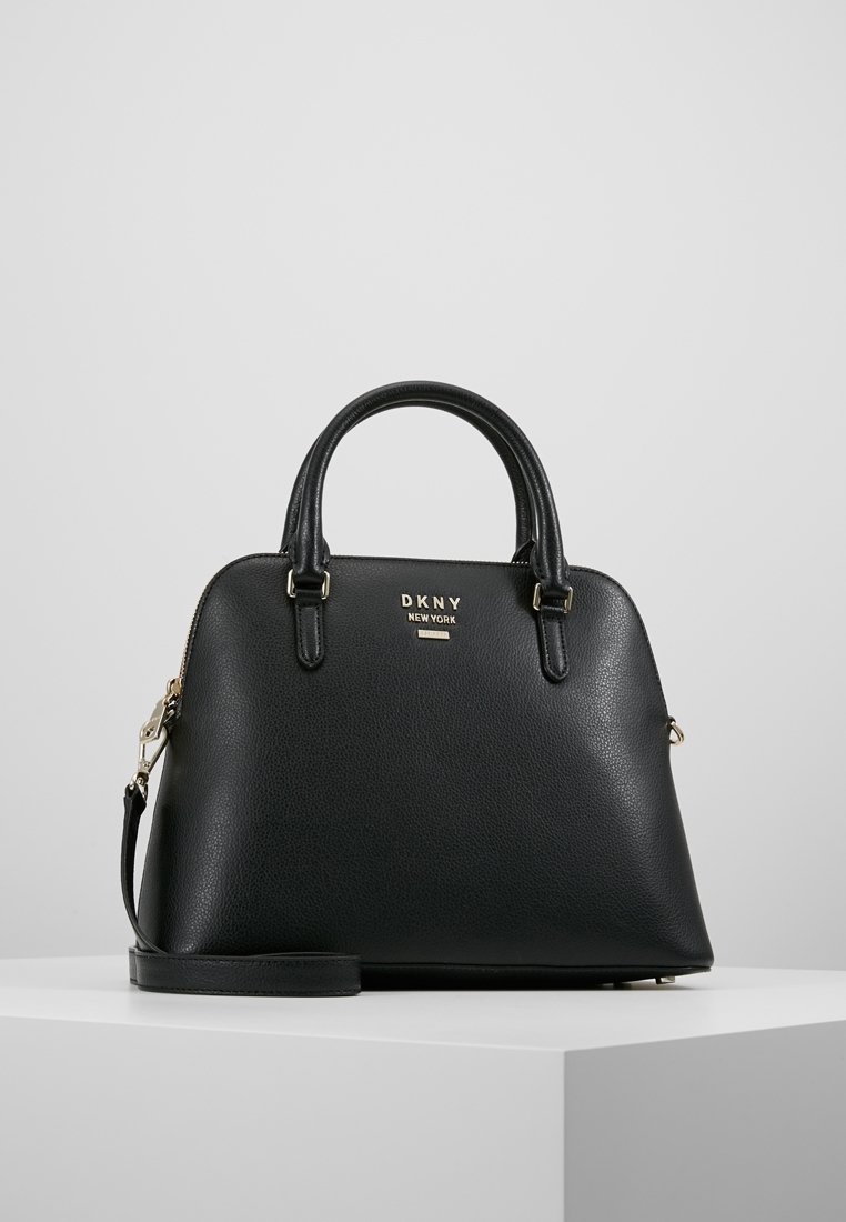 Černá strukturovaná kožená kabelka DKNY s dvojitými uchy, odnímatelným ramenním popruhem a zlatým logem na přední straně, umístěná na bílé ploše.