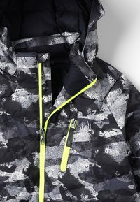 Lyžařská bunda s kamuflážním vzorem v odstínech černé a šedé, vybavená žlutým zipem a logem. Izolovaná, s kapucí a zipovými kapsami.
