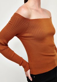 Schulterfreier, gerippter Strickpullover in verbranntem Orange mit langen Ärmeln und figurbetontem Schnitt. Verfügt über einen strukturierten Stoff und enge Bündchen.