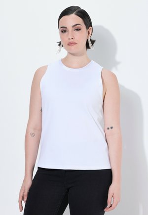 Top bianco senza maniche con scollatura rotonda, realizzato in tessuto morbido. La modella indossa jeans neri, mostrando tatuaggi sul braccio sinistro.