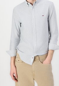 Pasiasta koszula zapinana na guziki w jasnoniebieskim i białym kolorze, wykonana z miękkiej bawełny. Posiada kołnierzyk i podwinięte rękawy, z małą naszywką z logo.