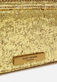 Gold glitter clutch bag featuring a textured surface, metallic accents, and an embossed logo plate. Smooth design with a rectangular shape.
