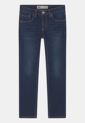 Jean skinny en denim bleu foncé avec des coutures dorées contrastantes, cinq poches et une ceinture dotée d'une fermeture à bouton et à glissière.