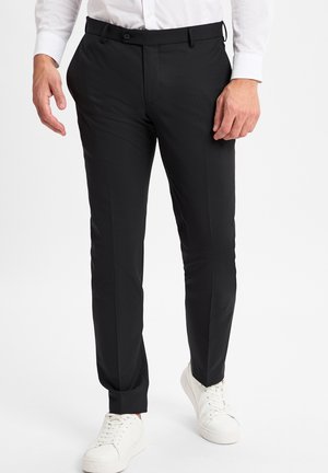 Schwarze Slim-Fit-Hosen aus einem glatten Stoff, mit flacher Vorderseite, seitlichen Taschen und einem schlichten Bund, kombiniert mit weißen Sneakers.