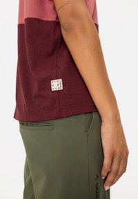Camiseta de manga corta bicolor en algodón rosa y burdeos con una etiqueta "BIOBASED". Pantalones verde oliva con un bolsillo lateral y un diseño elegante.