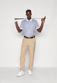 Ριγέ κοντομάνικο πόλο πουκάμισο σε μπλε και άσπρο, σε συνδυασμό με μπεζ παντελόνι. Ο παίκτης κρατάει ένα γκολφ κλαμπ· περιλαμβάνονται λευκά αθλητικά παπούτσια και μαύρη ζώνη.