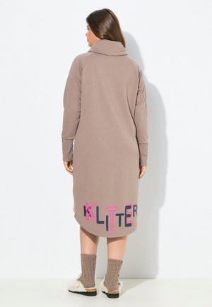 Lange beige jurk met een driekwart halslijn, voorzien van het woord "KLITTER" in kleurrijke letters aan de onderkant. Zachte textuur en een relaxte pasvorm.