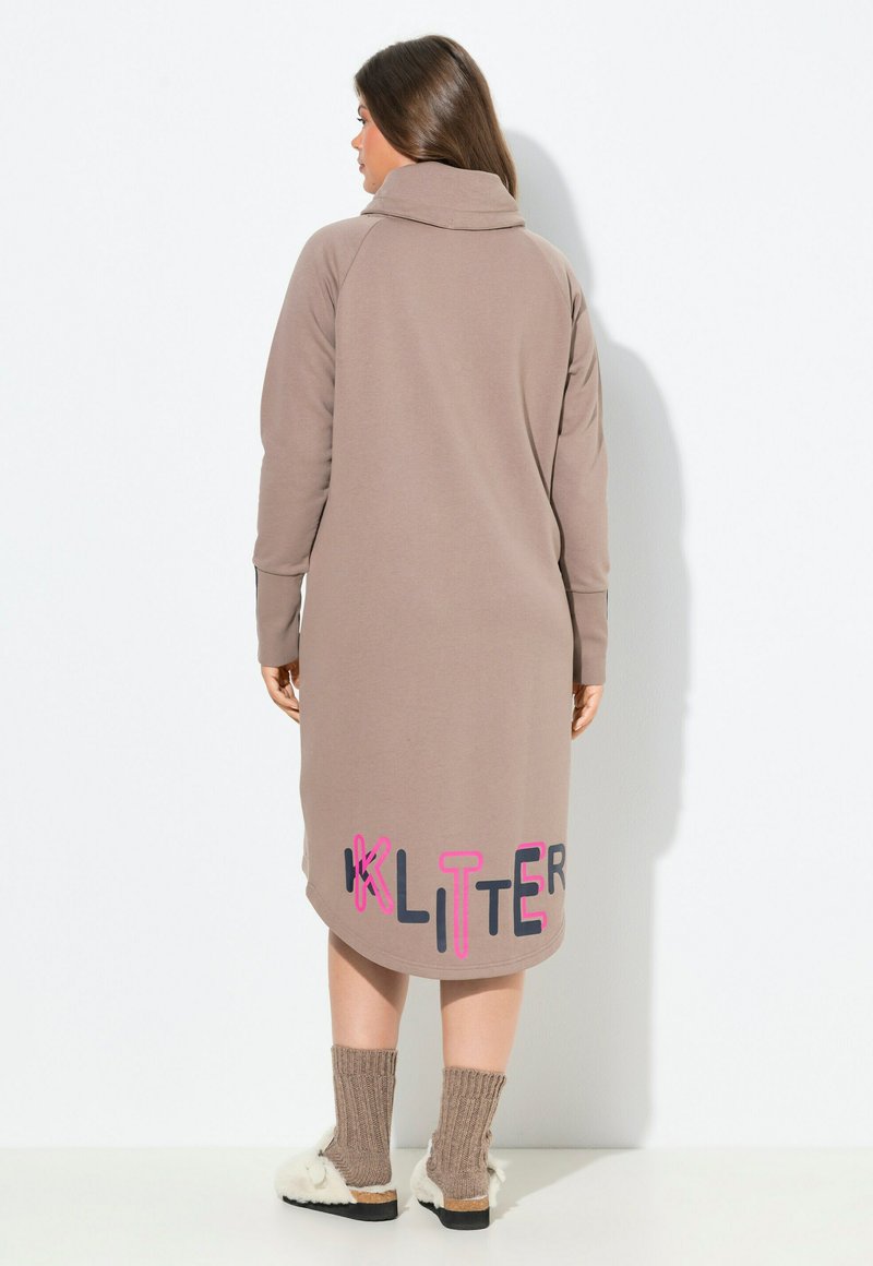 Pitkä beige mekko, jossa on cowl-kaulus ja helman alareunassa värikkäät kirjaimet "KLITTER". Pehmeä kangas ja rento istuvuus.