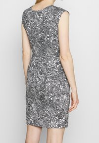 Robe sans manches noire et blanche avec un motif complexe paisley, une silhouette ajustée et une texture lisse. Vue de dos montrant un col rond.